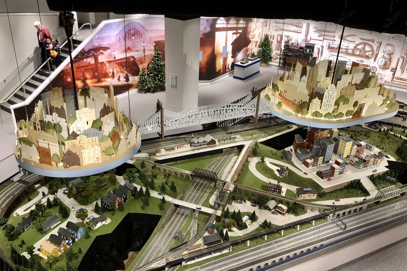 Dream Land installed at Holiday Junction: two suspended discs carrying Art Deco skylines of Cincinnati and Northern Kentucky, joined by the Roebling bridge, floating above the model train landscape