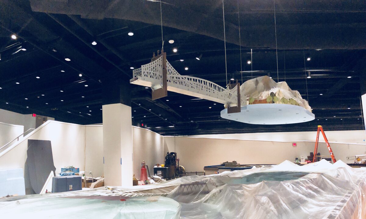 The skyline discs suspended mid-install, the Roebling bridge spanning between them, the exhibit hall still under construction below